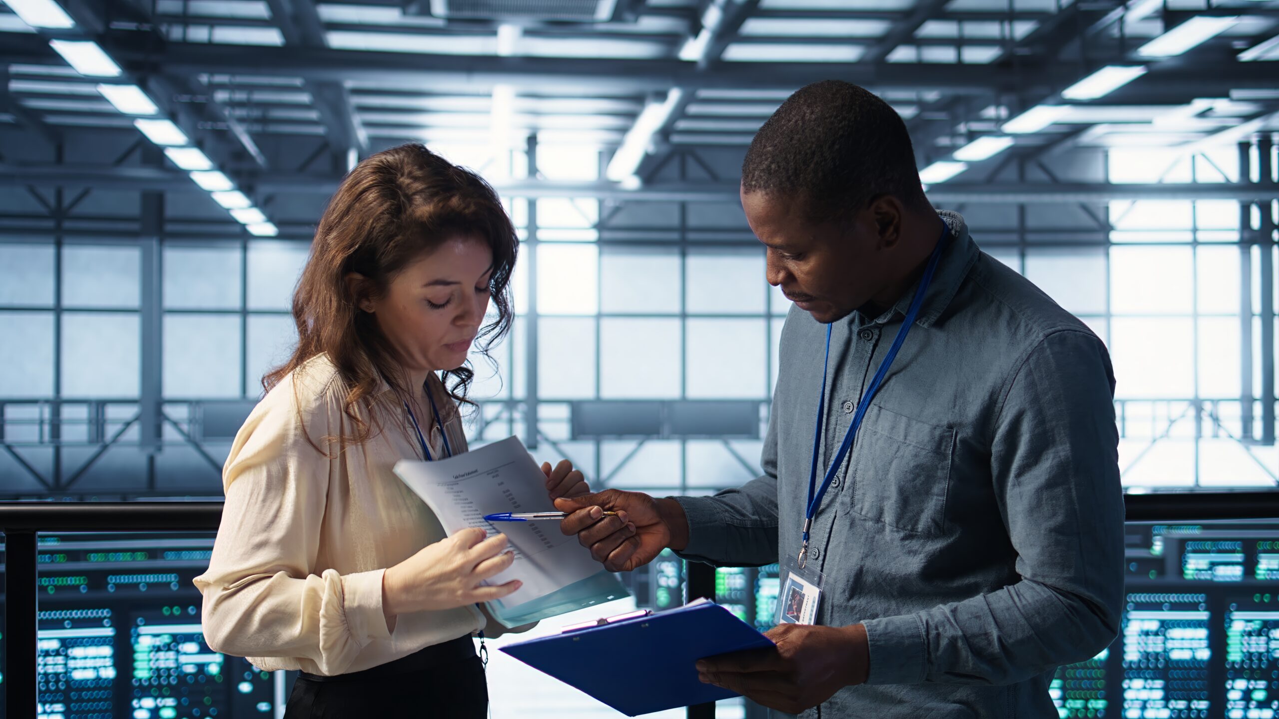 Two tech professionals wearing ID badges review data sheets in a modern server control room, illustrating the collaboration driving CI/CD in 2026 for faster and more reliable software delivery. Two tech professionals wearing ID badges review data sheets in a modern server control room, illustrating the collaboration driving CI/CD in 2026 for faster and more reliable software delivery.