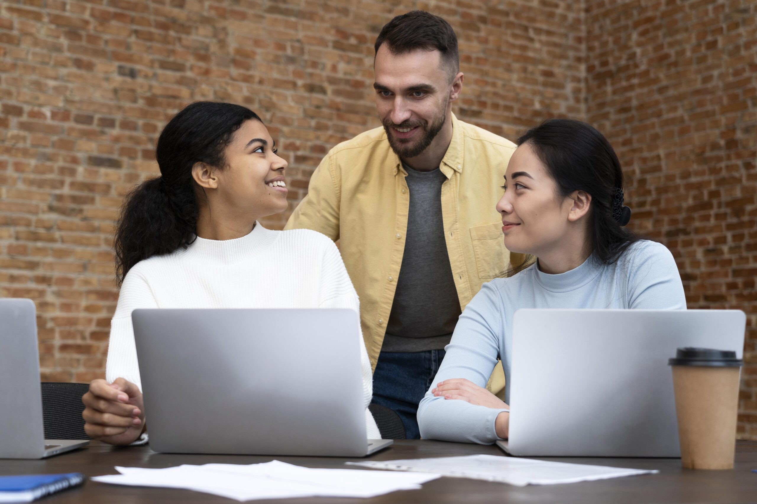Three diverse colleagues collaborate happily around laptops, illustrating the teamwork and confidence behind a Smooth, Secure & Smart Cloud Migration. Three diverse colleagues collaborate happily around laptops, illustrating the teamwork and confidence behind a Smooth, Secure & Smart Cloud Migration.