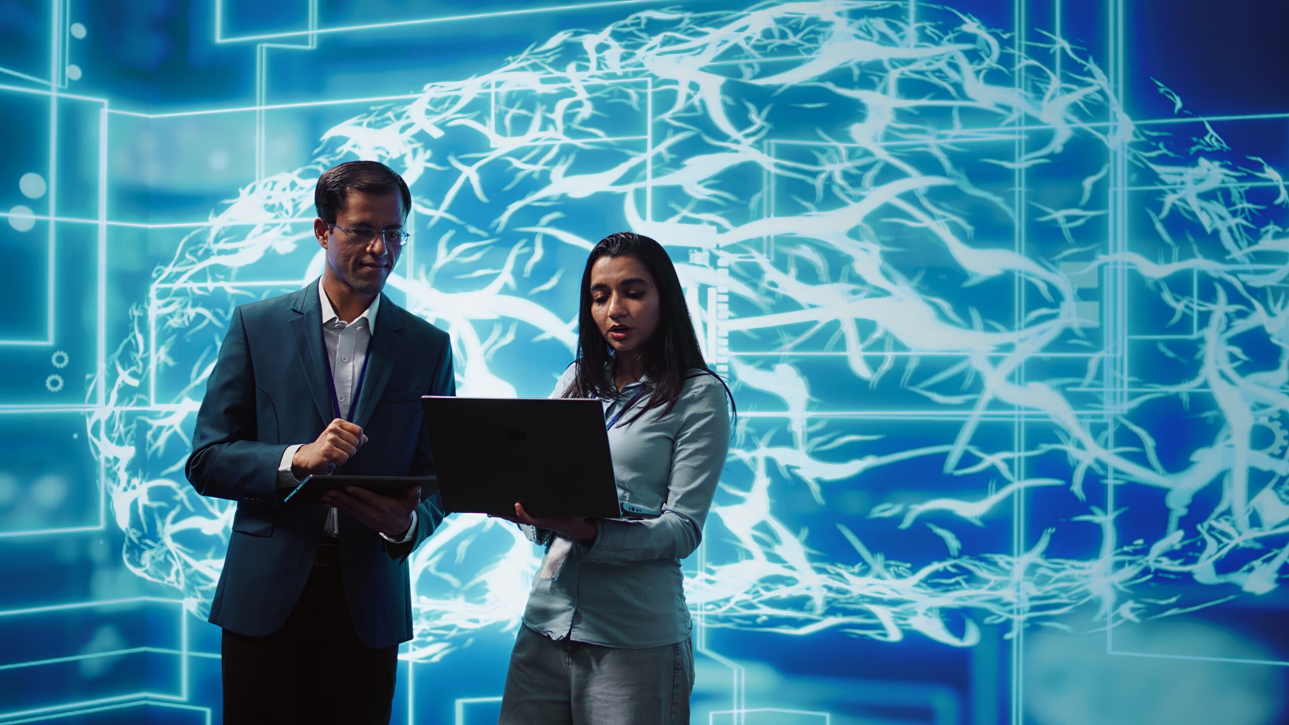 Two corporate professionals analyzing data on a laptop against a futuristic background featuring an illuminated neural network brain pattern, representing advanced cloud computing and artificial intelligence in business.