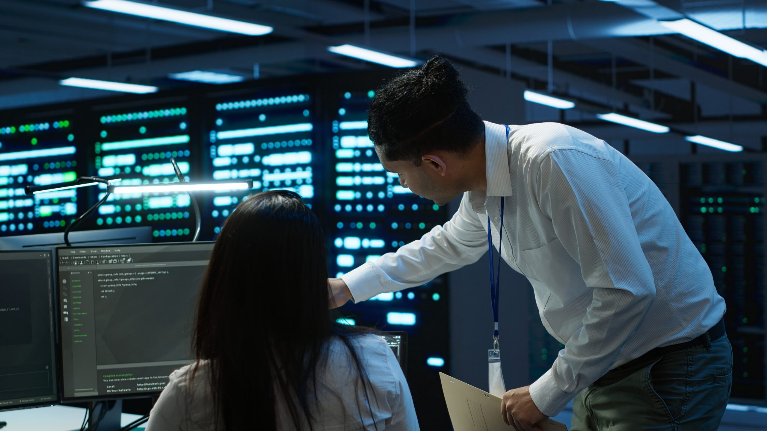Two enterprise security professionals reviewing cloud security configurations on monitors inside a server room, representing cloud security best practices for enterprise environments.