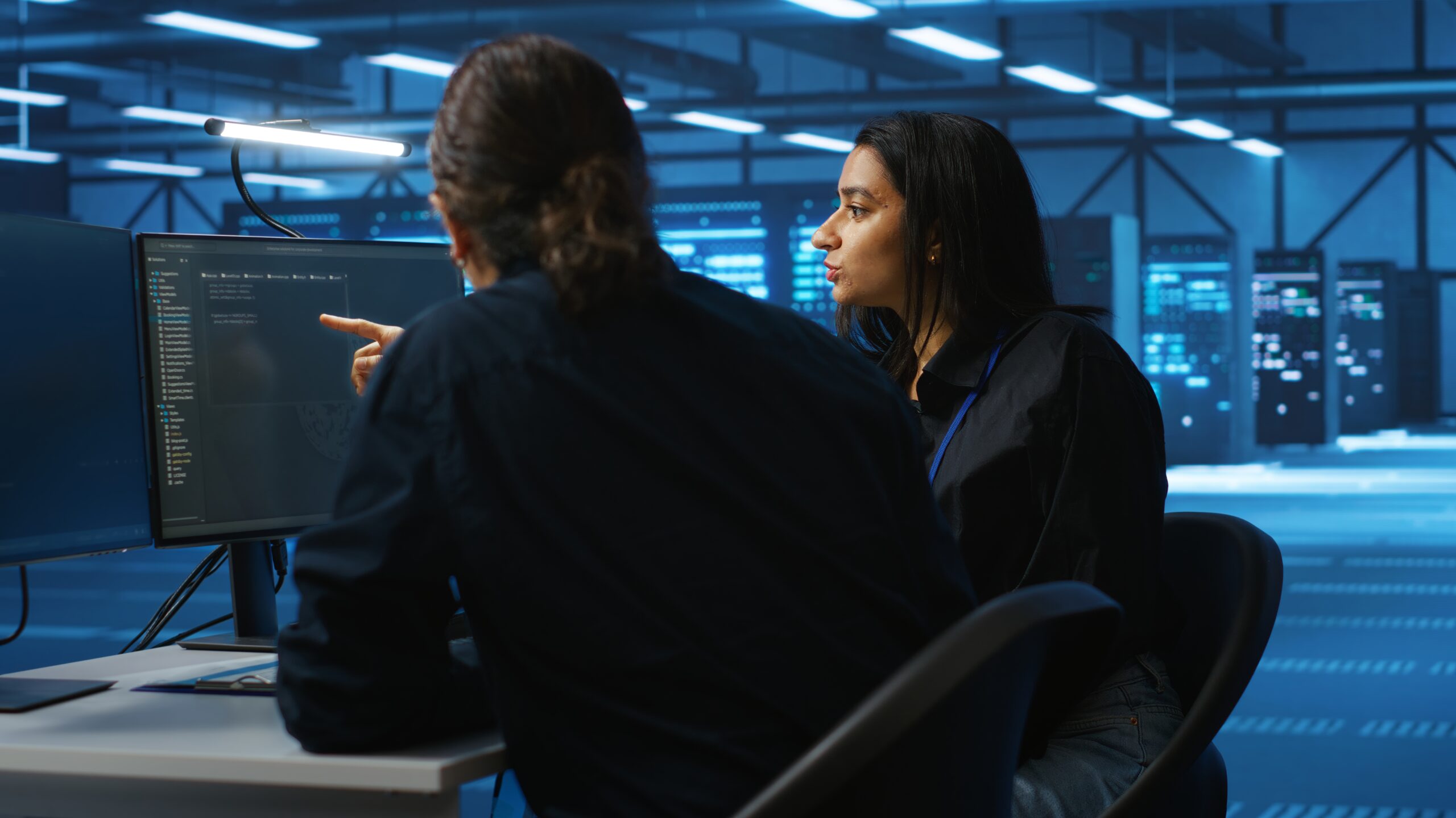 Two cloud engineers reviewing Kubernetes container orchestration configurations on a monitor inside a data center, representing a beginner's guide to Kubernetes and container orchestration by Sherdil Cloud.